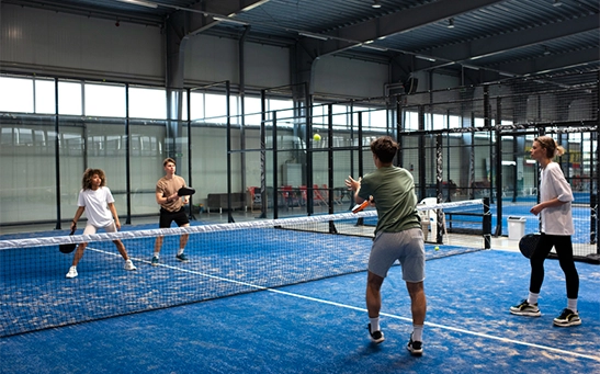 Padel game overview with players hitting ball in enclosed glass court